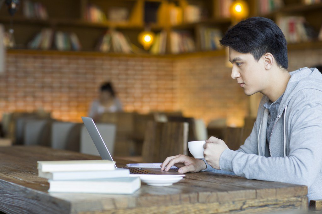 Student using a laptop in a cafe while wearing headphones, learning and searching the internet